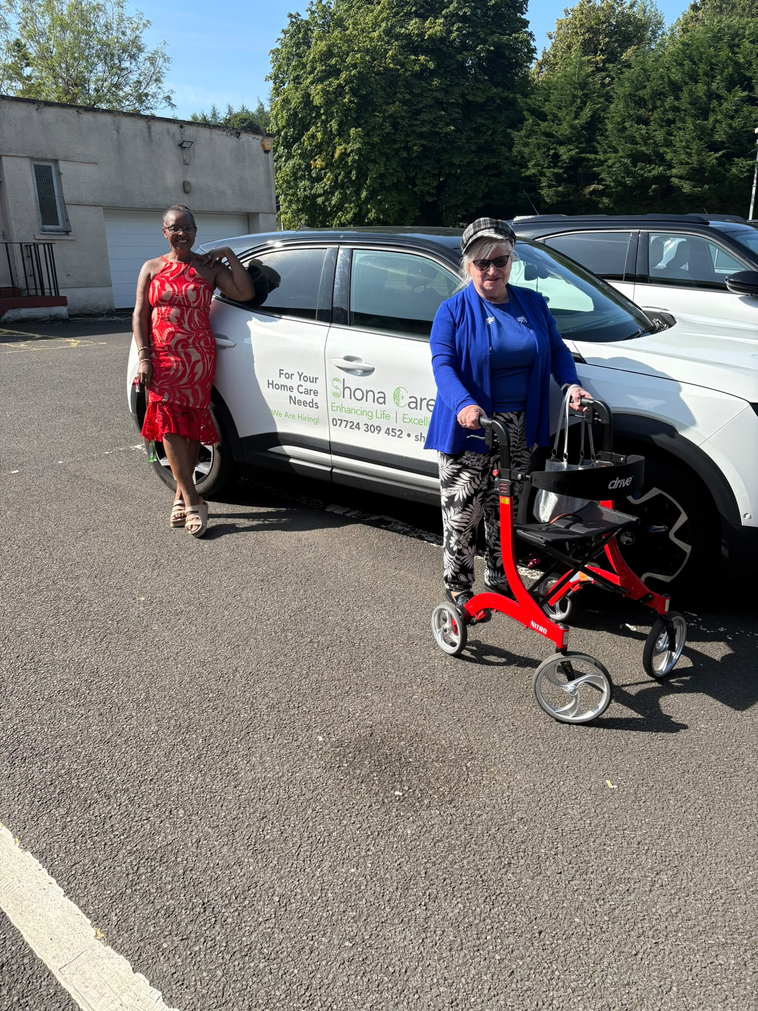 Val and Mrs B standing beside a Shona Care car outdoors.